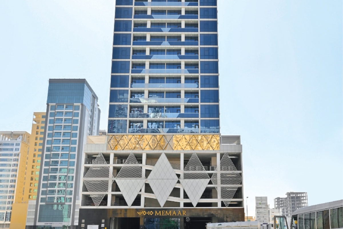 A modern high-rise building with glass windows and geometric designs on the facade, marked with the name "Memaar" at the entrance.