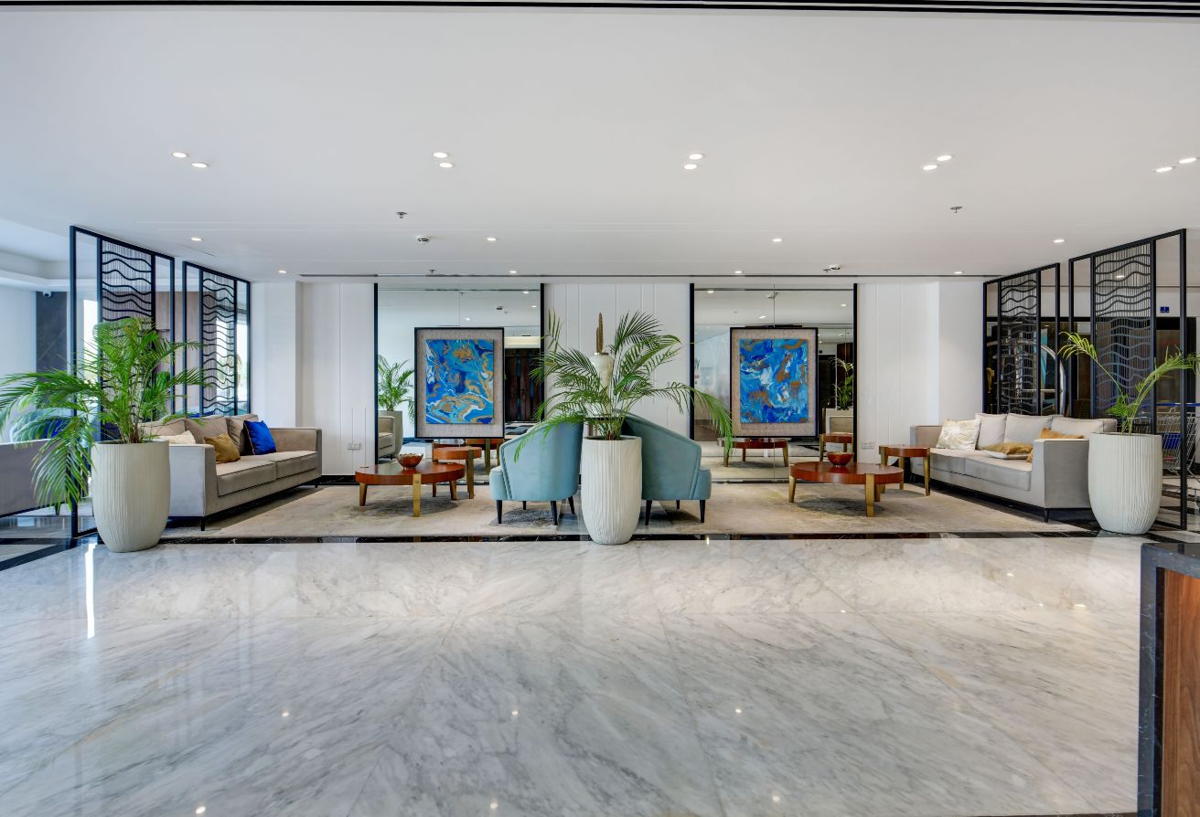 Modern Amwaj hotel lobby with marble flooring, contemporary seating, lush potted plants, and stunning abstract artwork gracing the walls—a signature Memaar design.