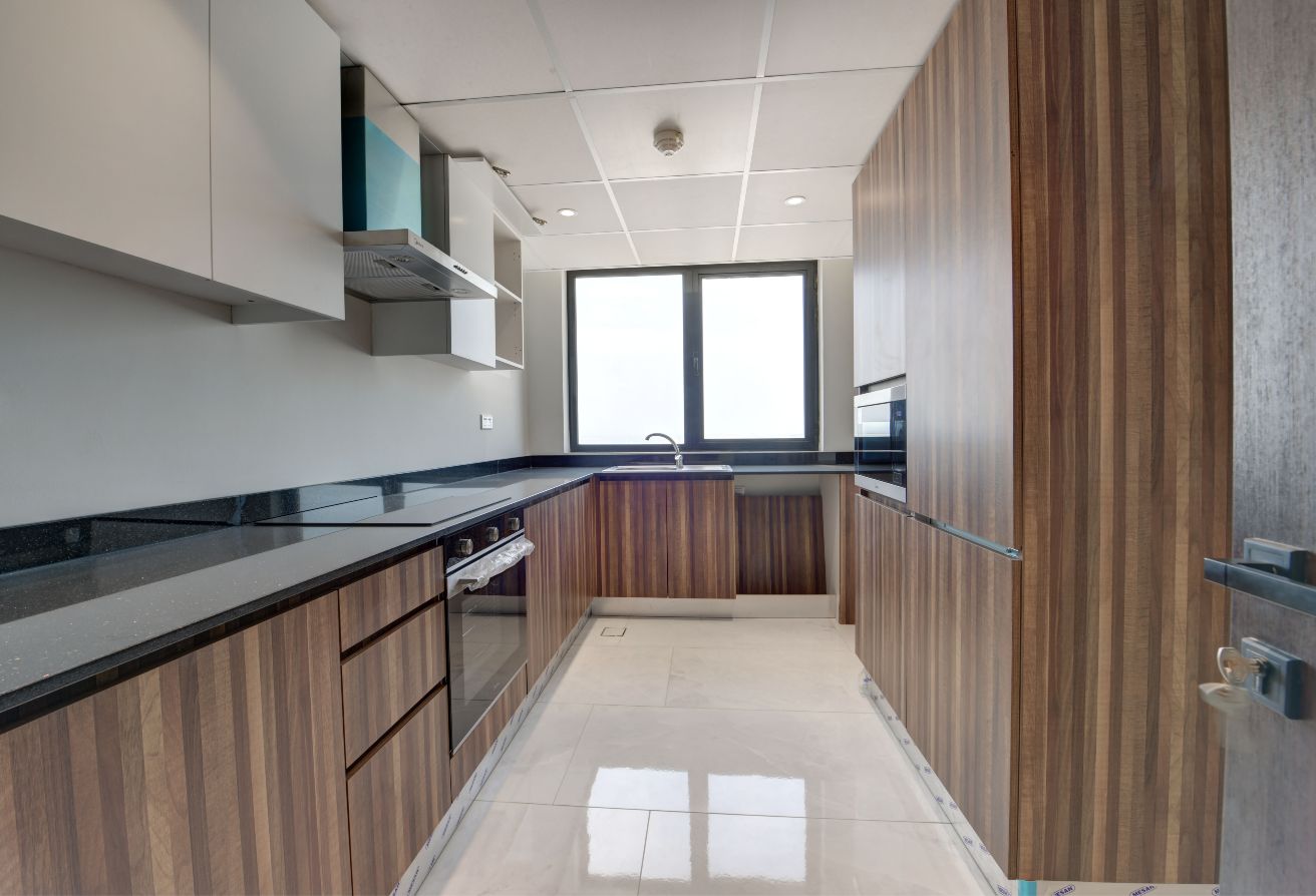Modern Amwaj kitchen with wood-paneled cabinets, black countertops, built-in oven, stove, and a large window providing natural light.