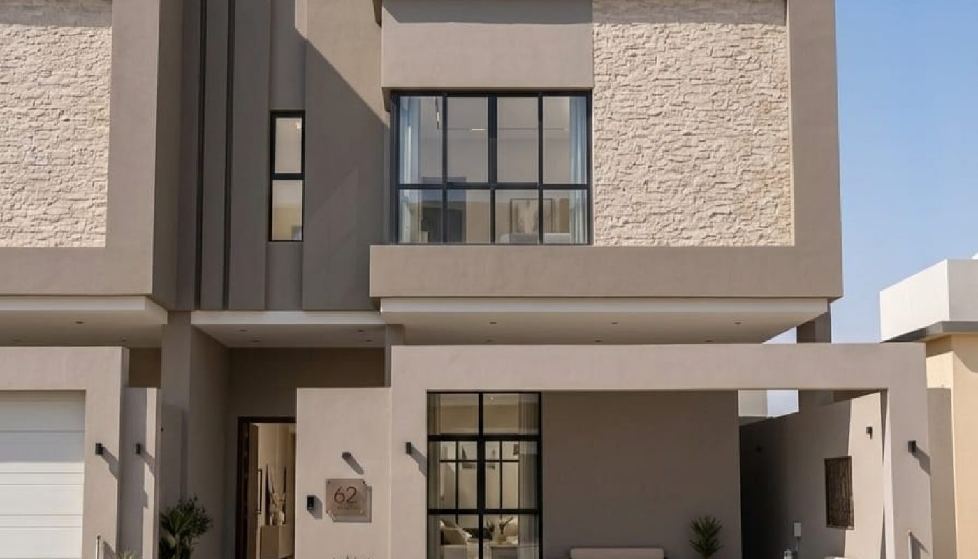 Modern two-story house with beige and stone facade, large windows, a small garden, and a carport under a clear blue sky.