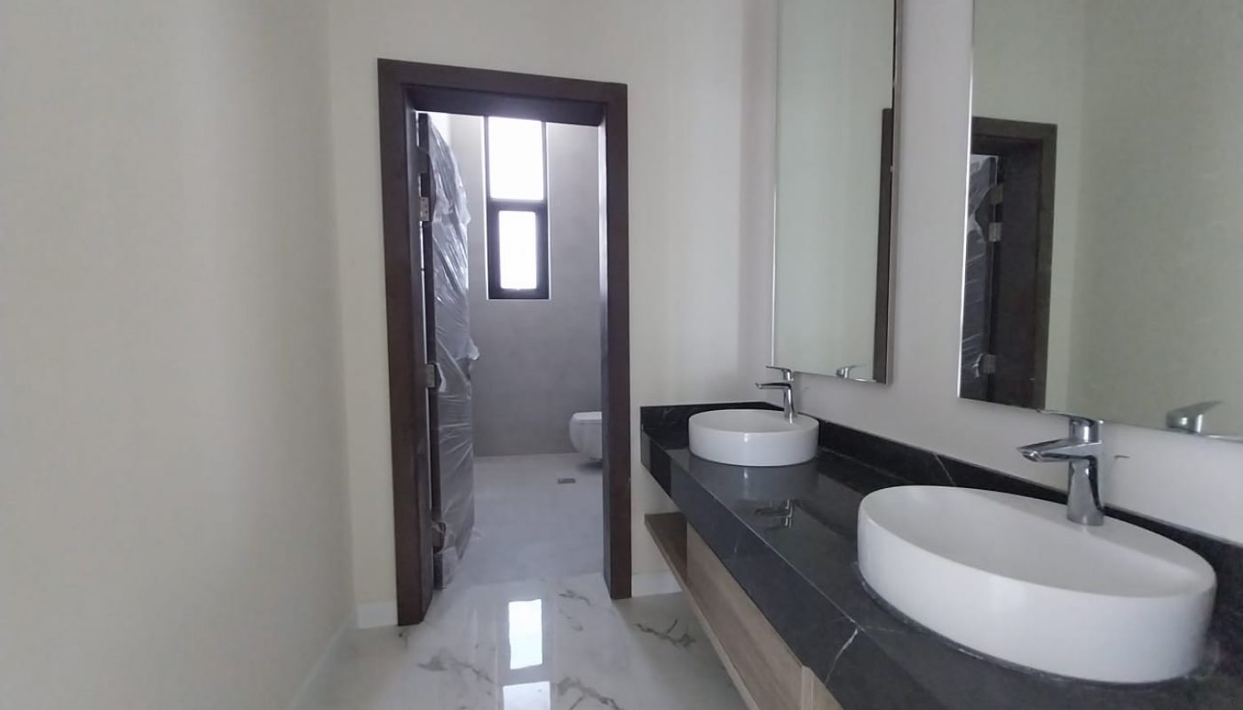 Bathroom with two round sinks on a black countertop, a large mirror, and a view of a separate toilet area through an open doorway.