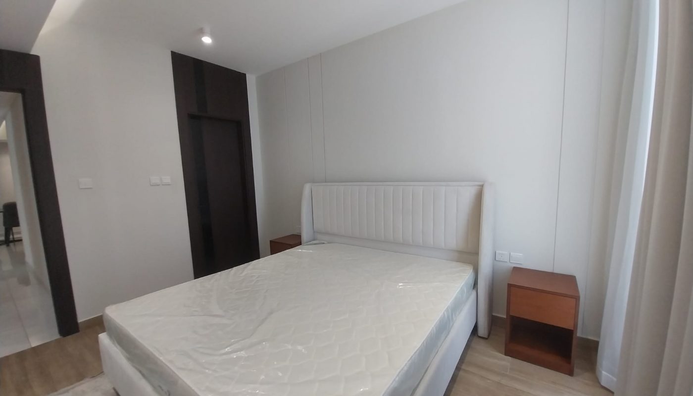 A minimally furnished bedroom with a double bed without bedding, two wooden nightstands, light walls, and a window with curtains.