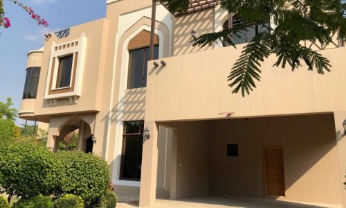 A luxury villa in Al Jasra available for rent, featuring beautifully landscaped gardens with lush bushes and trees adorning its front exterior.