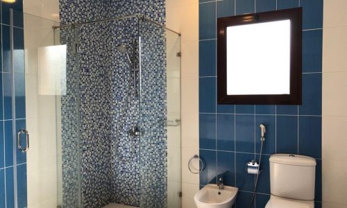 Rent a luxury villa in Al Jasra with a beautiful blue tiled bathroom featuring a toilet and shower.