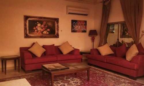Elegant villa for rent in Busaiteen with red sofas, a floral painting, ornate rug, and glass coffee table under warm lighting.