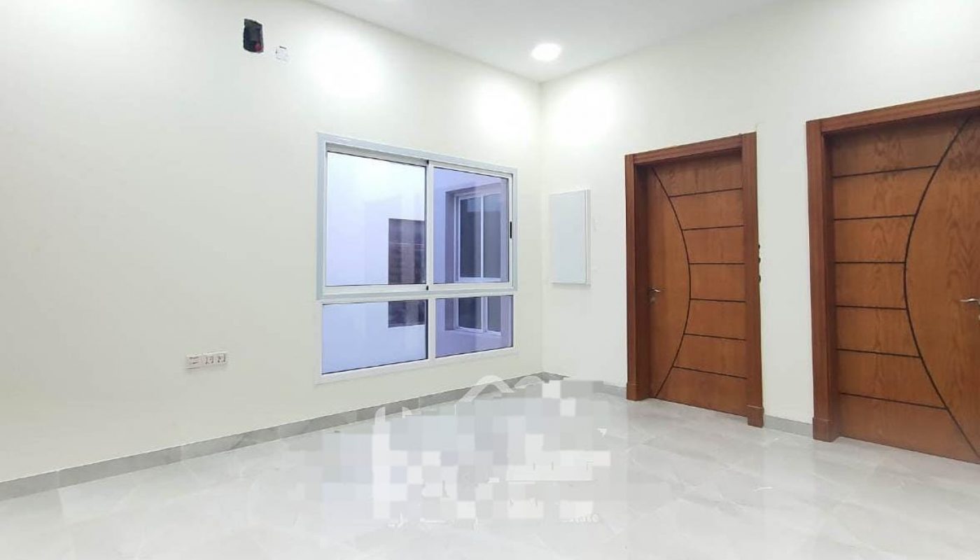 Empty room with white walls and tiled floor, featuring two wooden doors with curved designs, a window with a view of an internal space, and a ceiling fan with four lights.
