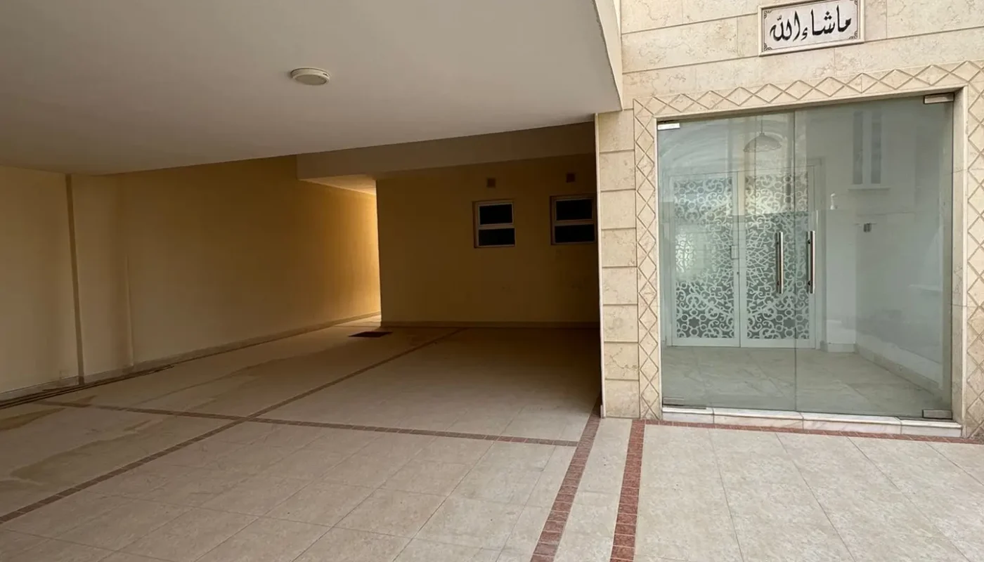Covered entryway with tiled flooring, glass doors on the right, two small windows at the back, and a sign with Arabic text above the entrance.