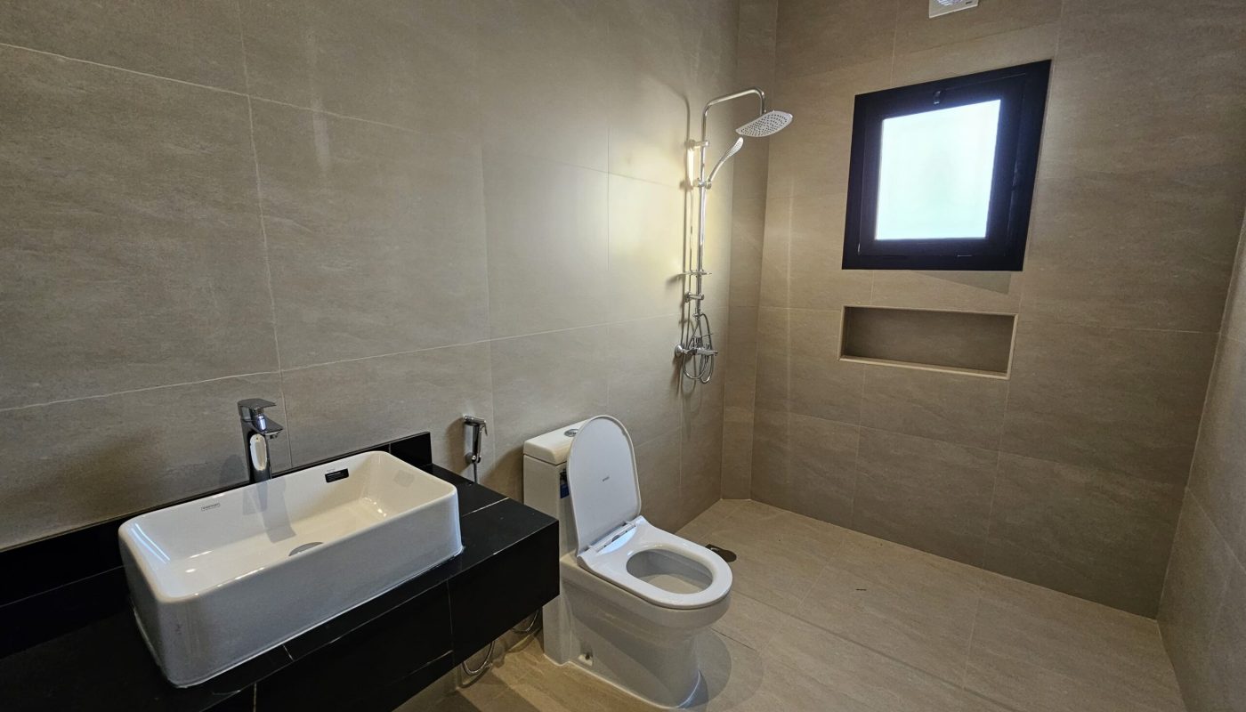 Minimalist bathroom with beige tiles, featuring a white toilet, sink with faucet, wall-mounted shower, and a small window.