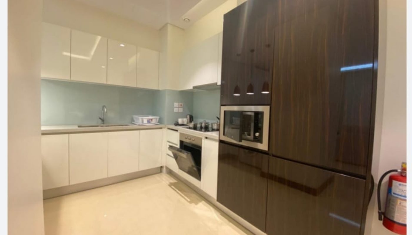 Modern kitchen with white cabinets, built-in oven and microwave, glossy dark wood paneling, light backsplash, and a fire extinguisher mounted on the wall.