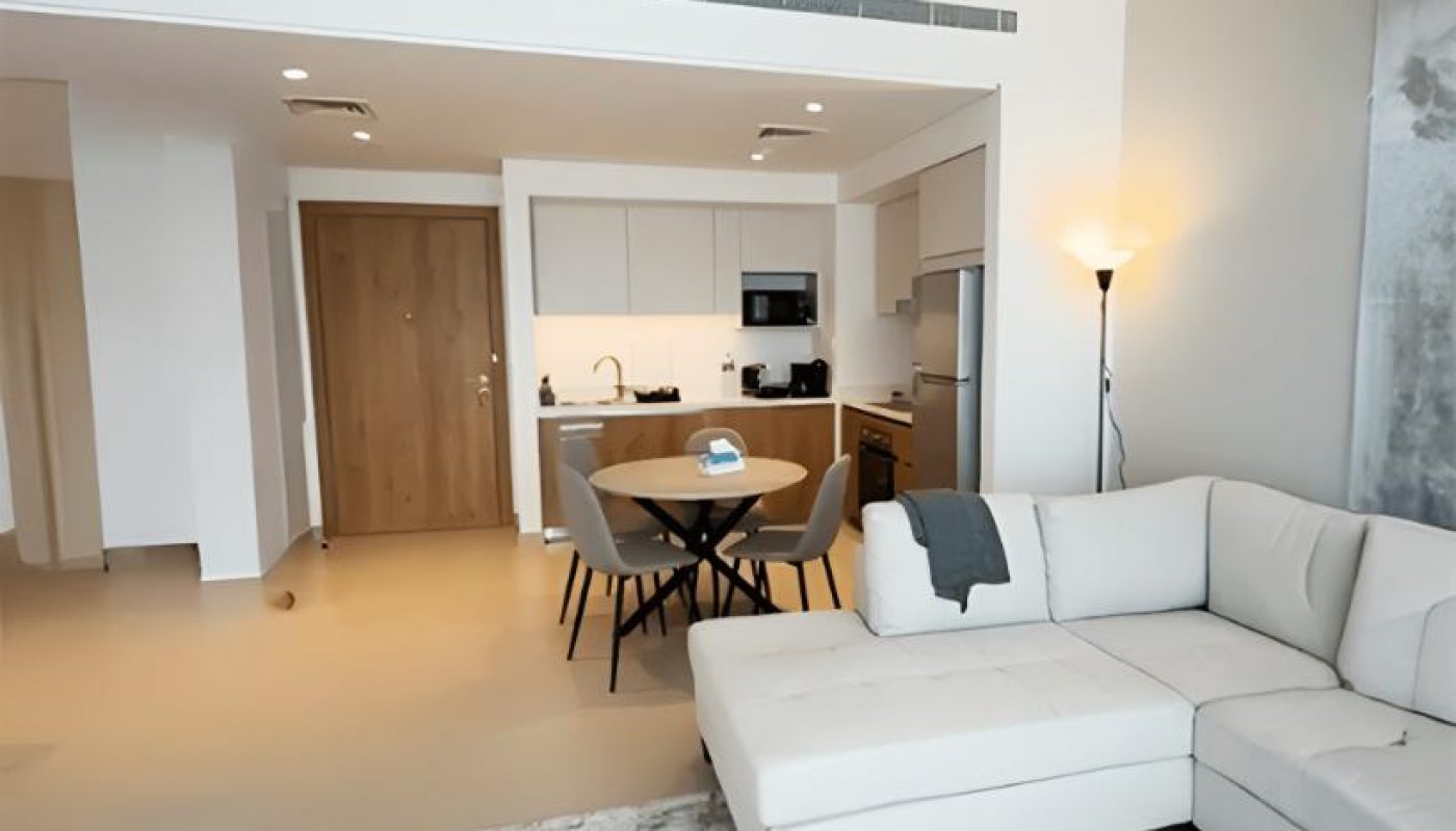 Modern open-plan living room and kitchen with a white sectional sofa, dining table, and neutral decor tones.