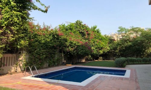 A luxury villa in Al Jasra with a backyard featuring a swimming pool and lush bushes.