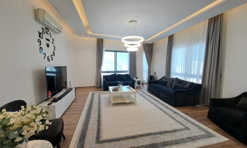 A luxurious living room with black furniture and a flat screen TV in a sale promo for an Al Janabiya luxury apartment.