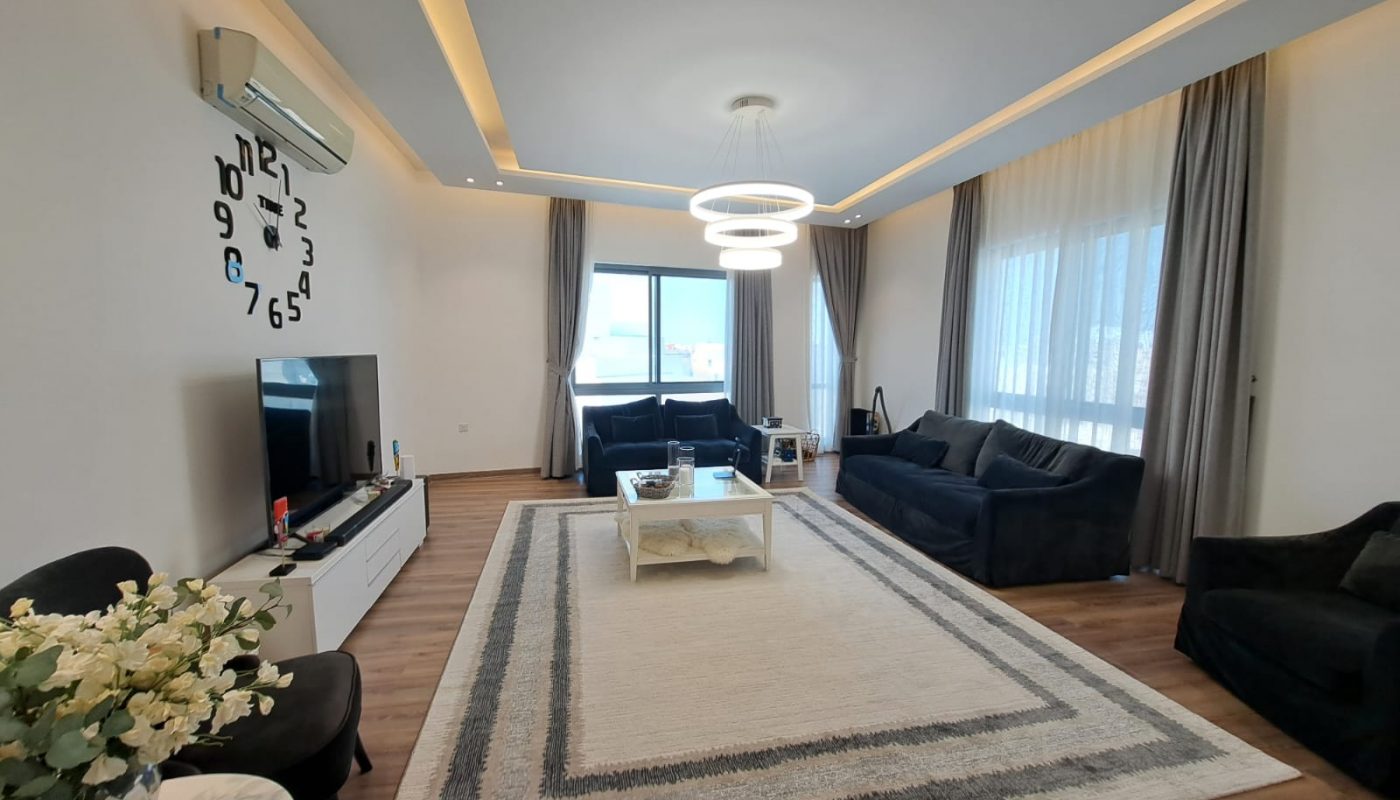 A luxurious living room with black furniture and a flat screen TV in a sale promo for an Al Janabiya luxury apartment.