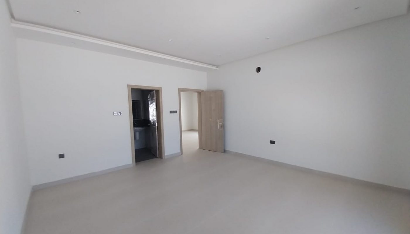 An empty, unfurnished room with white walls, a beige tiled floor, and two open doorways; one door is partially open and leads to another room.