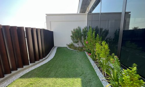 A small garden with grass and plants in front of a luxury building.