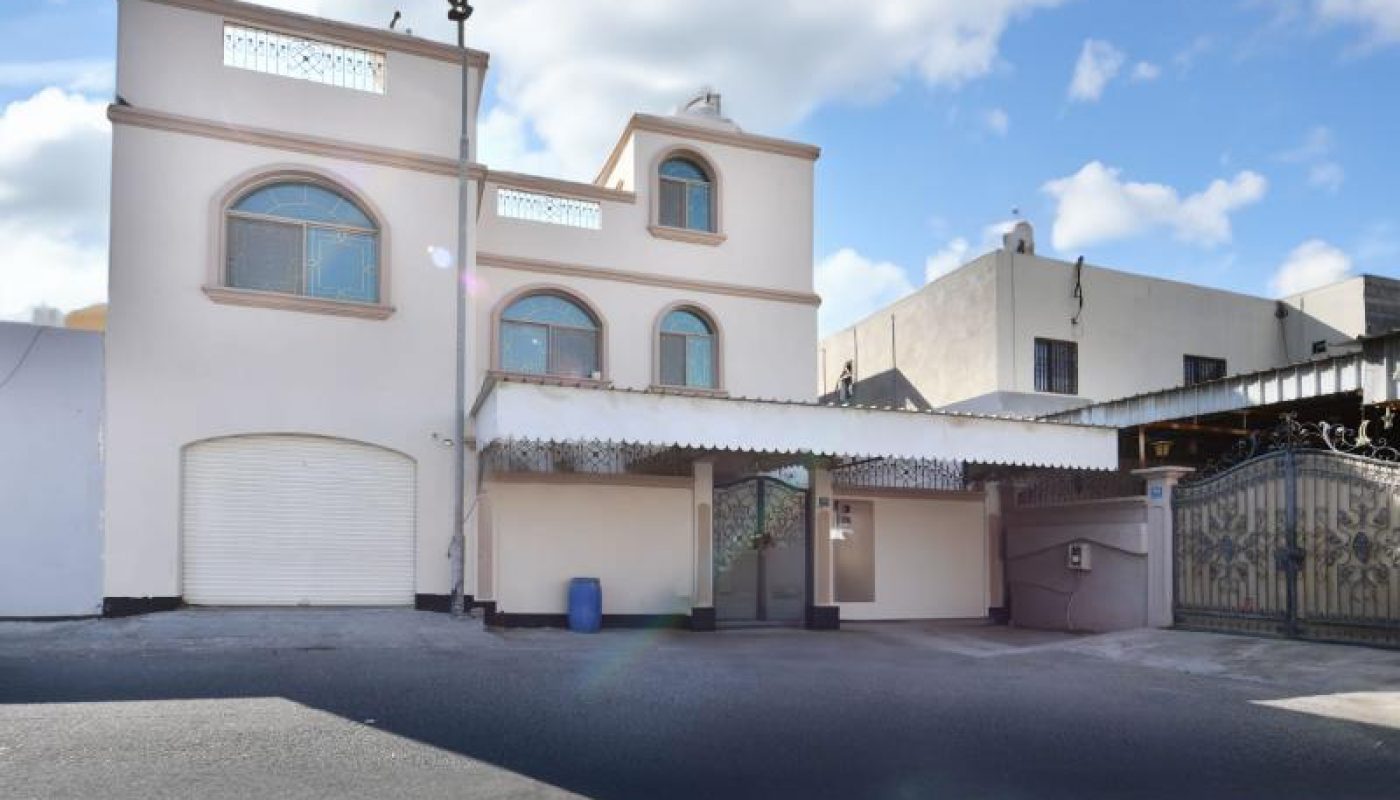 Two-story white house with arched windows, a garage, and a covered carport, set against a partly cloudy sky.