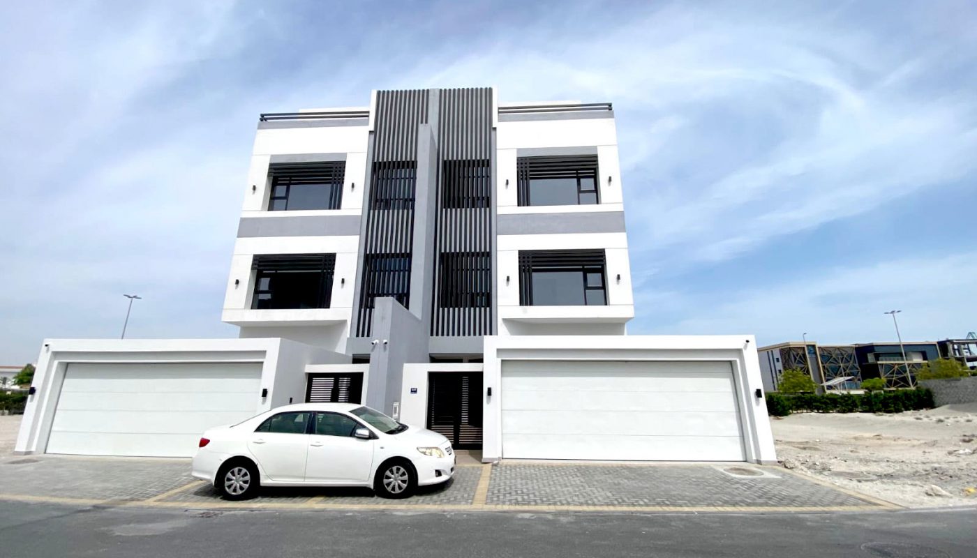 A modern, white three-story building with two garages and a parked white car in front, set on a paved street under a partly cloudy sky.