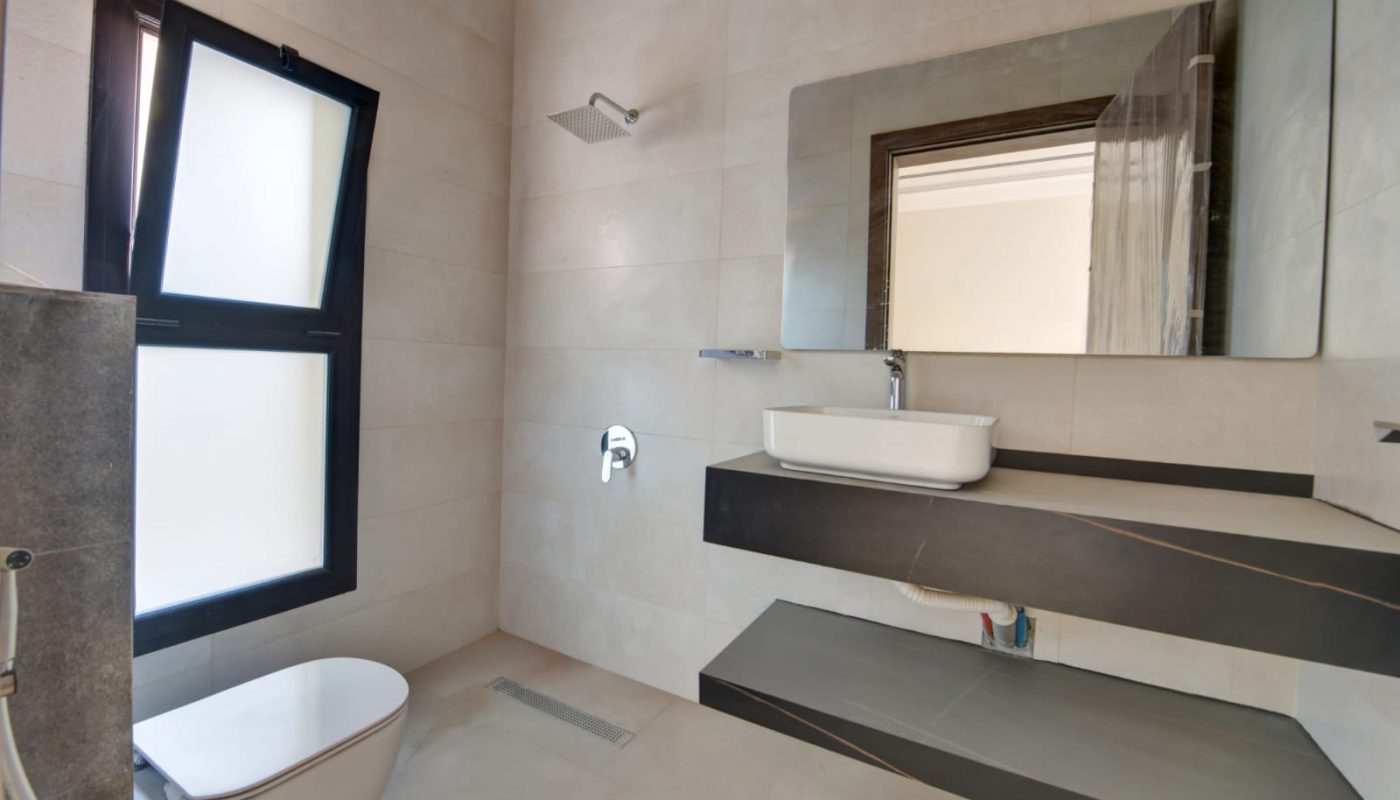 Modern bathroom with a wall-mounted toilet, frosted window, large mirror, vessel sink on black floating counter, and light beige tiles.