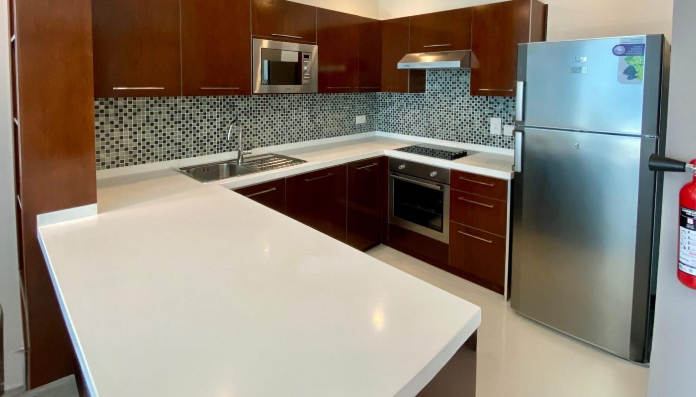 Modern kitchen with brown cabinets, white countertops, stainless steel appliances, mosaic tile backsplash, and a built-in oven.