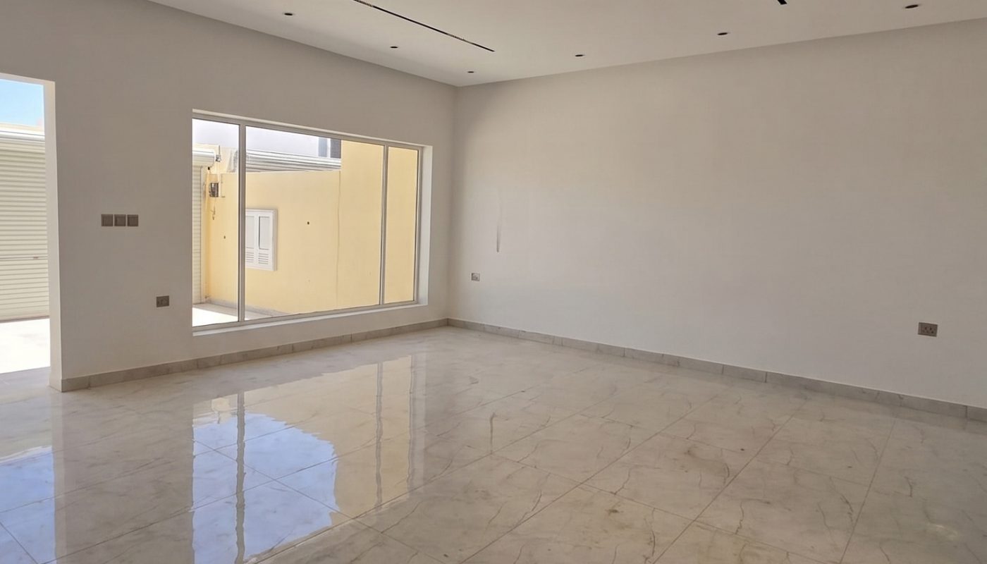 Spacious empty room with marble tile flooring, white walls, recessed ceiling lights, and large windows letting in natural light.