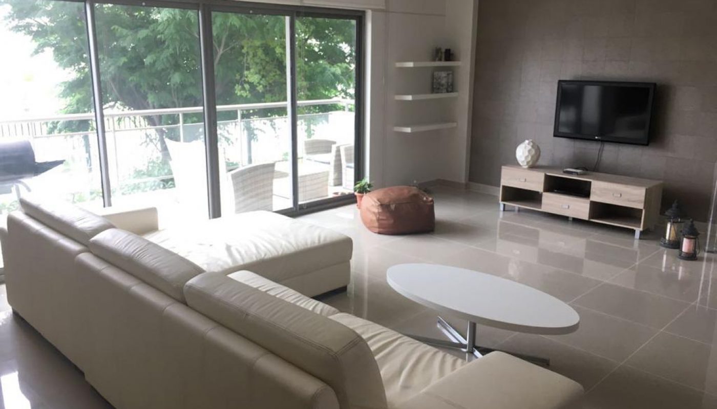 A fully furnished living room in an Amwaj Islands apartment with a white couch and TV available for rent.