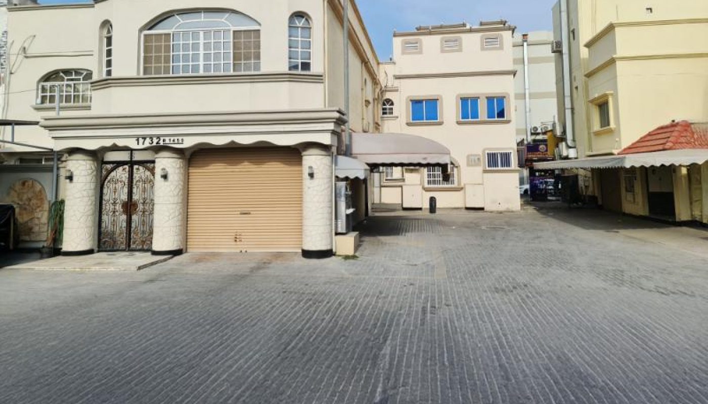 A paved driveway leads to multiple beige and white buildings with closed garages and windows under a partly cloudy sky.