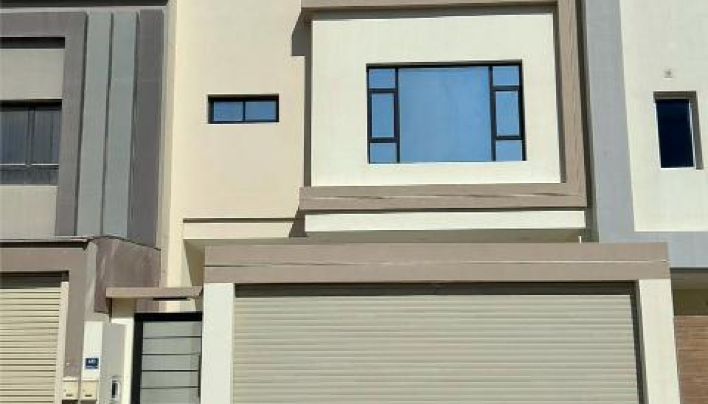 Modern two-story house with a flat roof, large garage door, and rectangular windows under a clear blue sky.