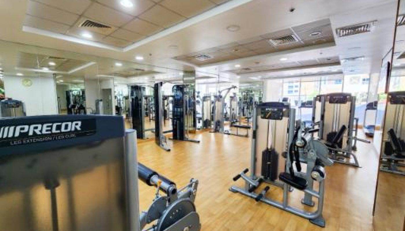 A spacious gym with wooden floors, mirrors on the walls, and various strength training machines neatly arranged throughout the room.
