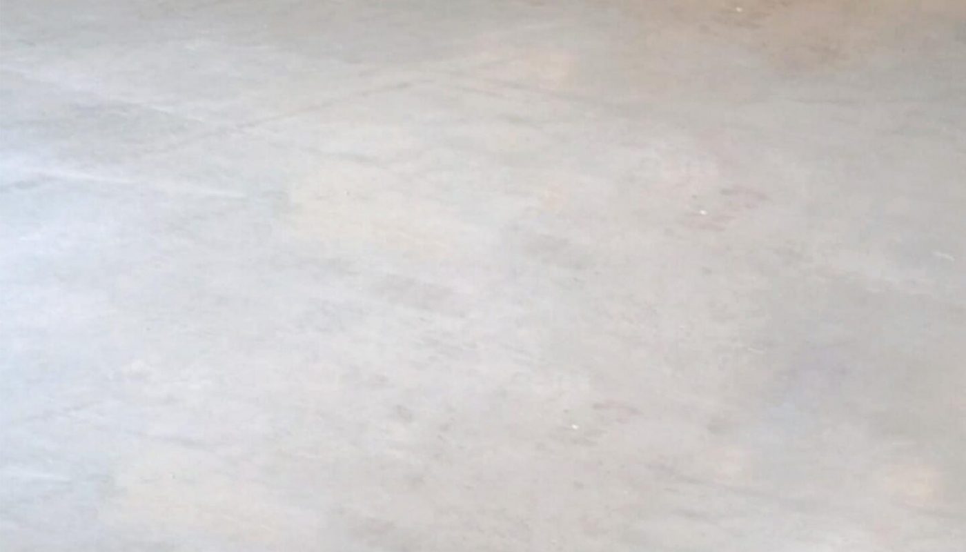 Empty warehouse with concrete floor, metal walls, and a red door in the corner under fluorescent lighting.