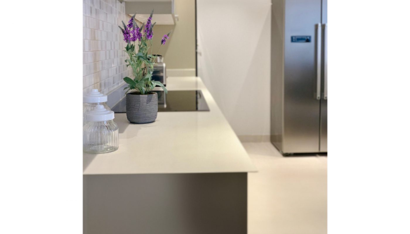 Modern kitchen with a beige countertop, a potted plant, glass jars, a stovetop, and a stainless steel refrigerator in the background.