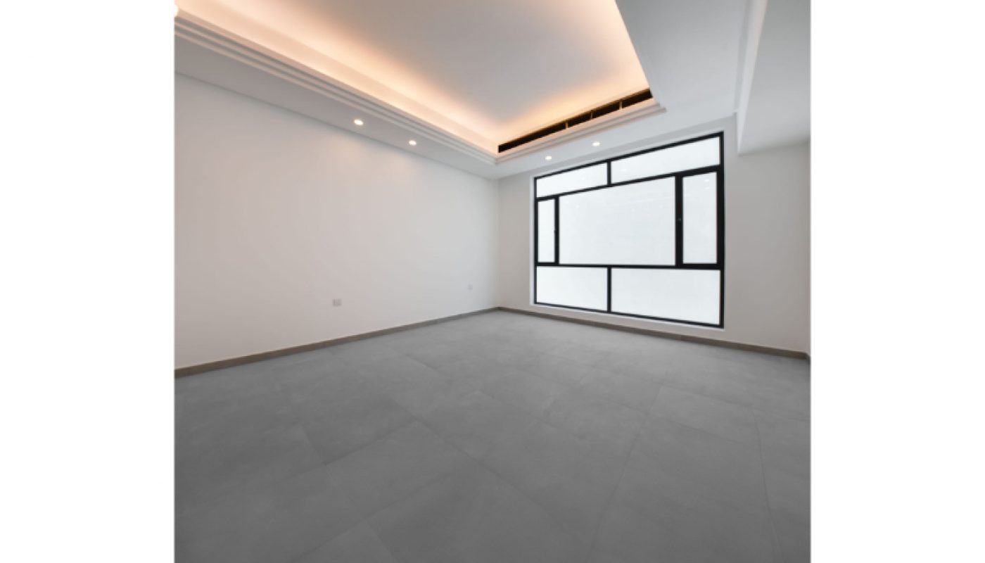 Empty modern room with gray tiled floor, white walls, a large geometric window, and recessed ceiling lights with cove lighting.