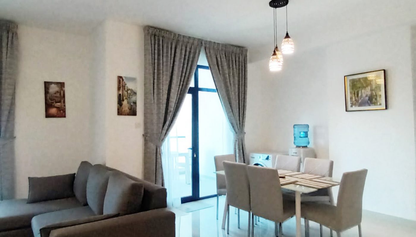 Modern living and dining area with grey sofa, six-seat dining table, tiled floor, large window with curtains, hanging lights, and framed pictures on white walls.