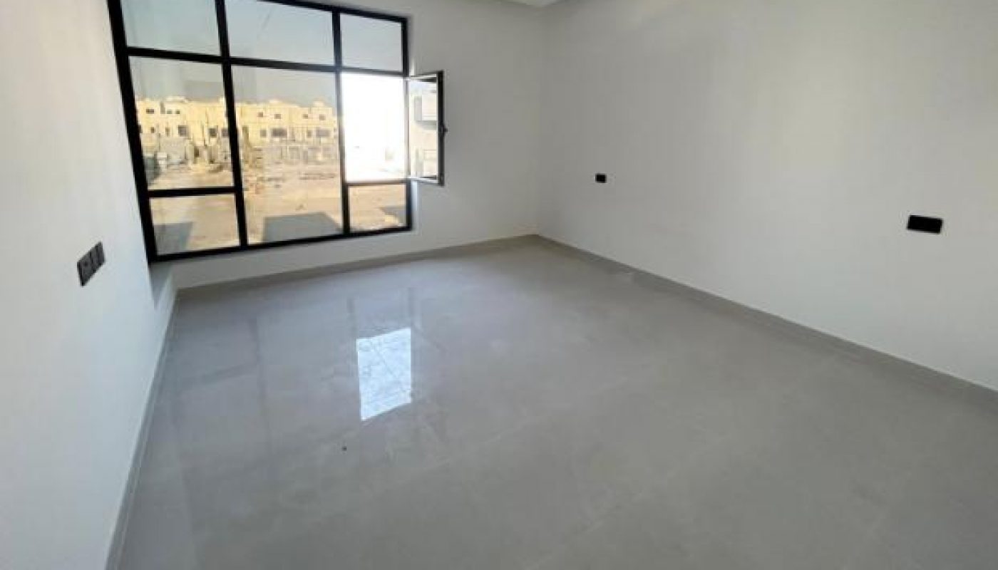 Empty room with white walls, large window, gray tiled floor, and ceiling lighting fixture. One window pane is open, and buildings are visible outside.