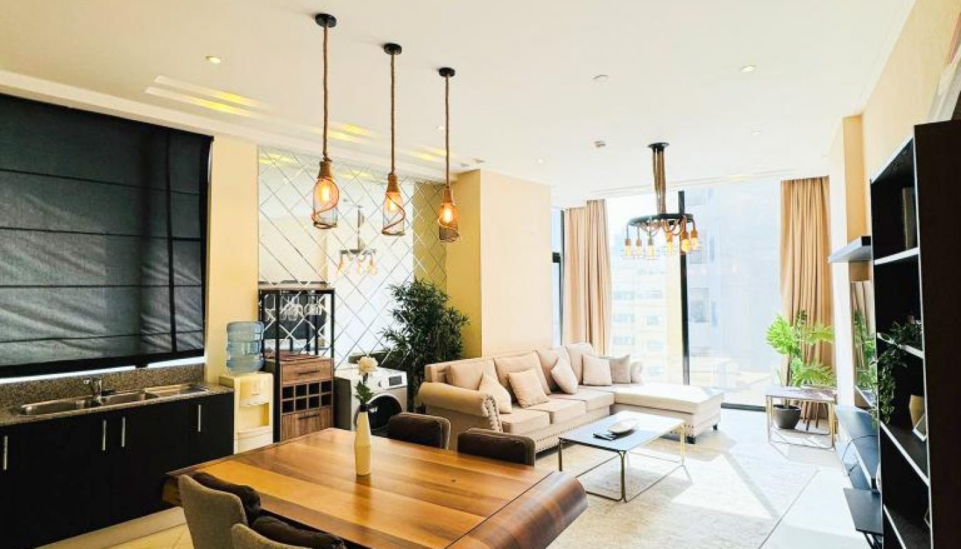 Modern open-plan living and dining area with a wooden table, beige sofa, floor-to-ceiling windows, and pendant lights, featuring neutral tones and contemporary decor.