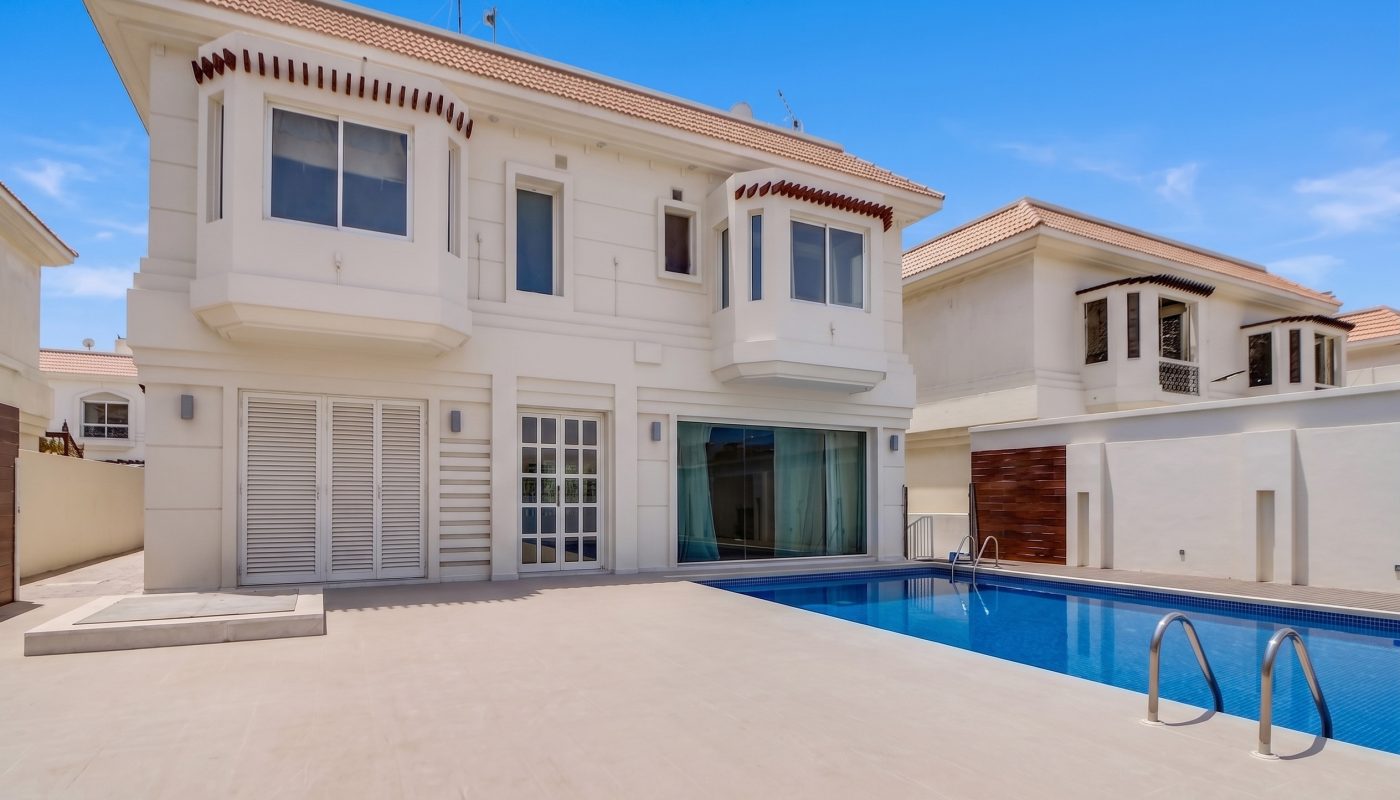 Modern two-story white house with large windows, outdoor patio, and a rectangular swimming pool under a clear blue sky.