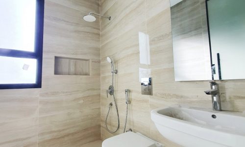 A modern bathroom with beige tiled walls featuring a toilet, sink, mounted mirror, shower, and a small window. With its clean lines and minimalist design, the space feels both organized and contemporary—almost as if it were created by auto draft.