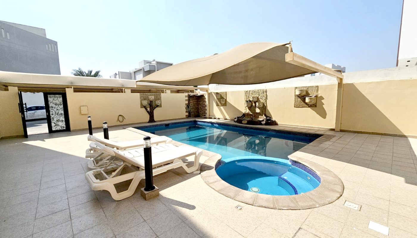 Outdoor pool area with a small round hot tub, several white lounge chairs, beige tiled flooring, and cream-colored walls under a canopy.