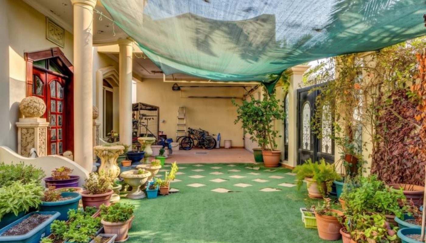 A covered outdoor patio with potted plants, artificial grass flooring, and several bicycles in the background near a house entrance.
