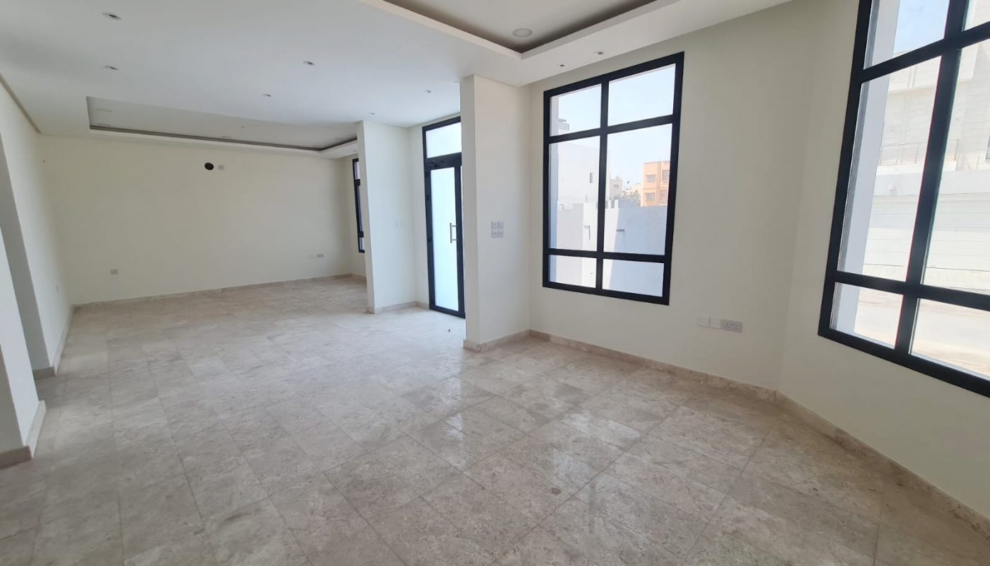 Empty, unfurnished room with large windows, tiled floor, white walls, and ceiling lights, illuminated by natural light.