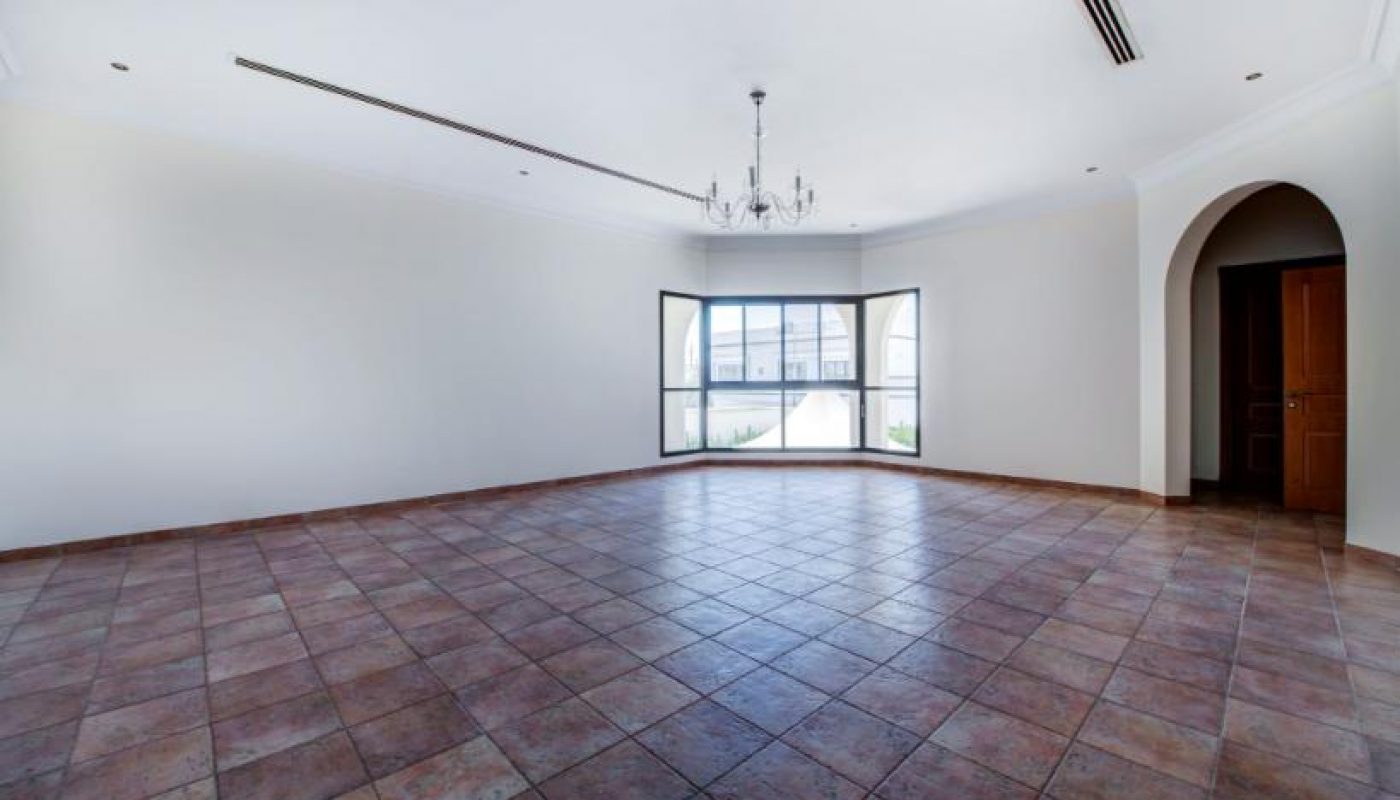 Spacious empty room with tiled floor, white walls, chandelier, large window, and arched doorway.