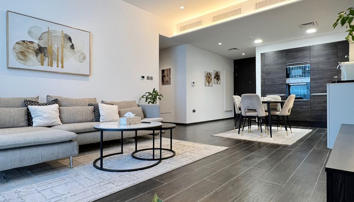Modern open-plan living and dining area with gray sofa, abstract wall art, round coffee tables, and dining table; plants and neutral decor accents are visible.