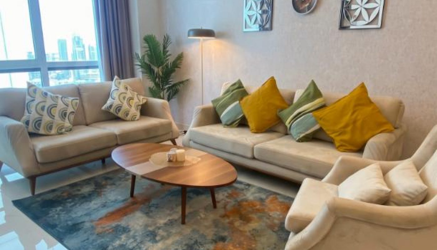 Modern living room with two sofas, an armchair, coffee table, decorative pillows, wall art, a potted plant, floor lamp, and large window with city view.