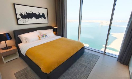 A spacious bedroom in a fully furnished apartment with a bed and a stunning view of the water.