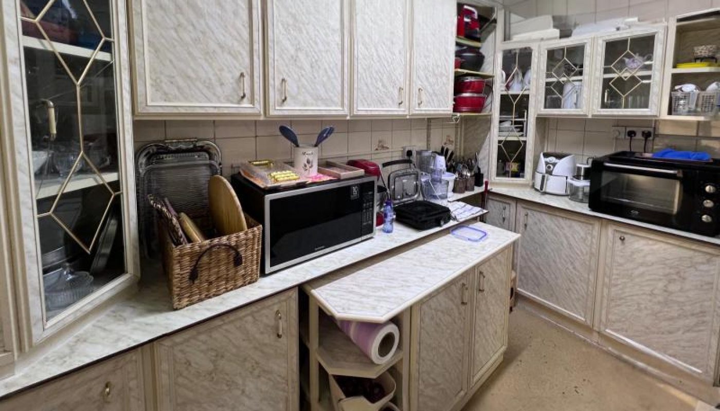 A kitchen with white cabinets, a microwave, a dish rack, paper towels, a toaster oven, and various dishes and appliances on the counters.