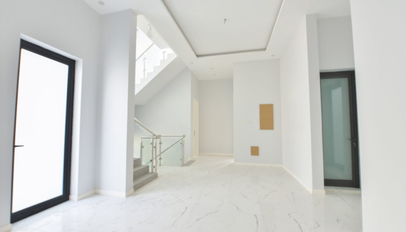 Bright, modern, empty interior space with white walls, marble floors, glass stair railing, and black-framed doors.