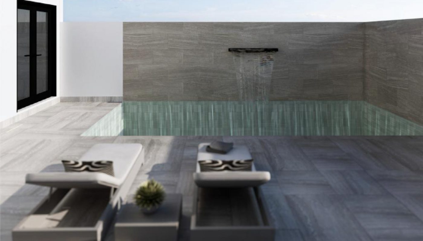 Modern minimalist courtyard with a small rectangular pool, waterfall feature, two white lounge chairs, and a small potted plant on a stone-tiled patio under a clear blue sky.