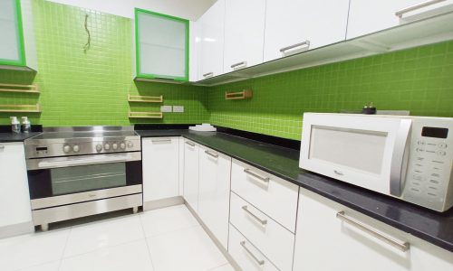 A spacious kitchen with green walls and white appliances in a luxury apartment for rent in Seef.