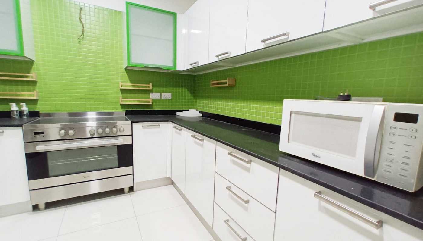 A spacious kitchen with green walls and white appliances in a luxury apartment for rent in Seef.