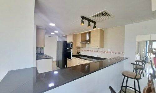 An apartment kitchen with black counter tops and bar stools.