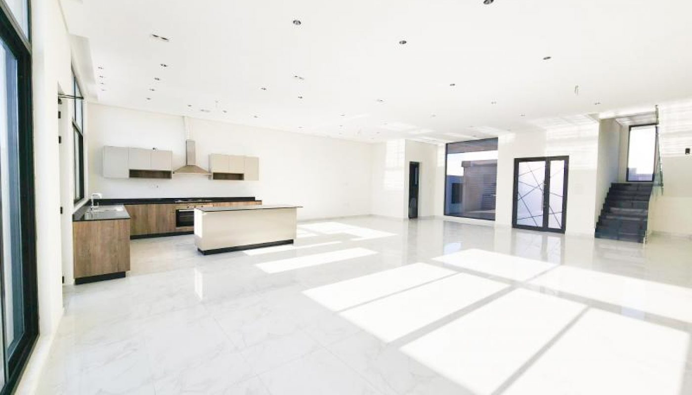 Spacious, modern open-plan kitchen and living area with large windows, white walls, marble floors, and a staircase leading upward.